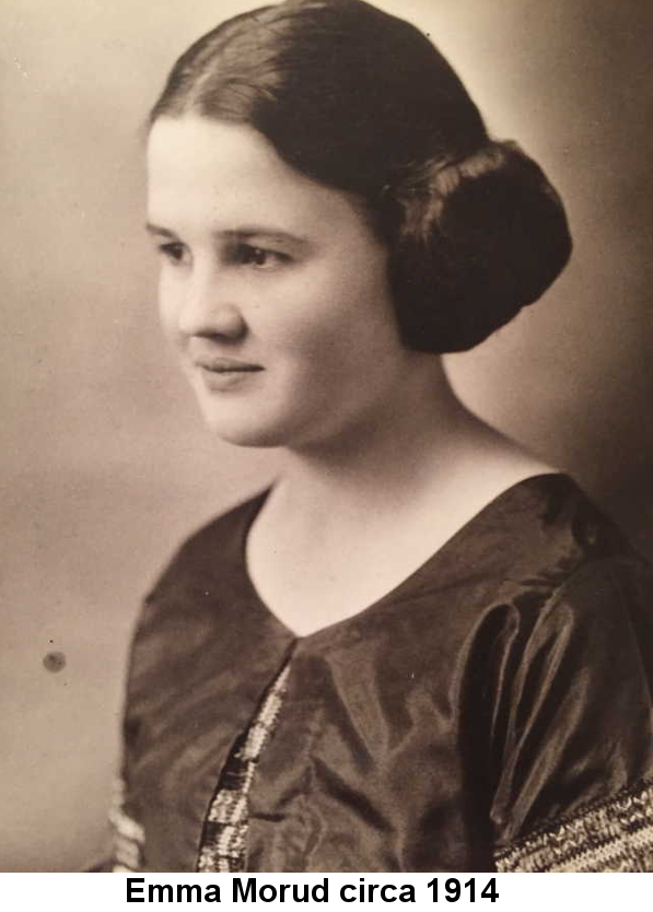 Sepia-tone studio portrait photo of a girl in her early teens, dark hair pulled into tight buns on either side of a center part; wearing a satin blouse and looking toward the left.